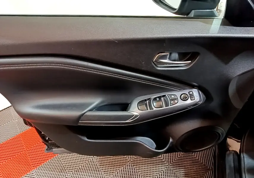 Vue intérieure du côté gauche de la porte avant noire du Nissan Juke Hybrid 143 Business+ avec commandes de vitres et rétroviseur.