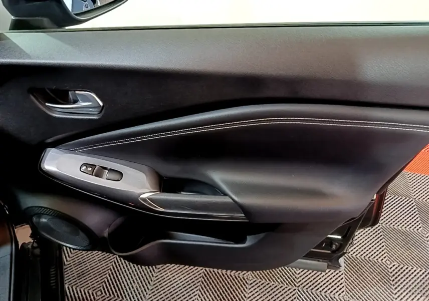 Vue intérieure du panneau de porte côté gauche noir avec commandes de vitres et poignée argentée du Nissan Juke Hybrid 2022.