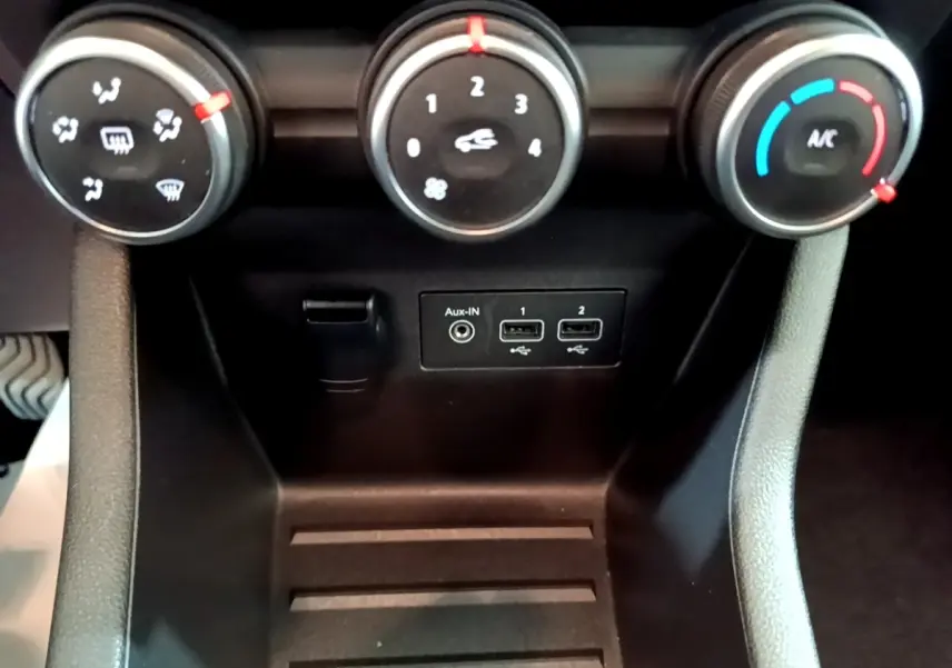 Gros plan sur les commandes de climatisation et les ports USB/Aux d’une Renault Clio Evolution SCe 65, intérieur noir.