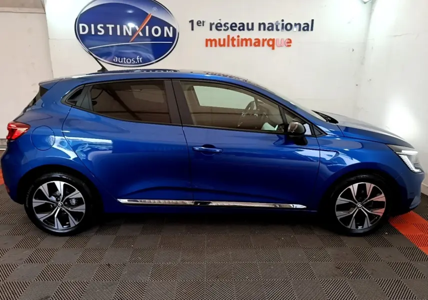 Profil droit d'une Renault Clio bleu 2022 avec jantes alliage et vitres teintées, dans un showroom intérieur.