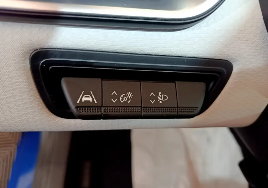 Gros plan sur les boutons de réglage des aides à la conduite dans une Renault Clio bleu, intérieur clair.