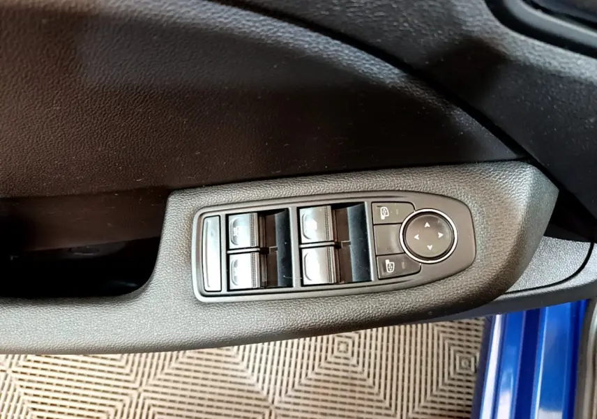 Gros plan sur les commandes de lève-vitres et réglage des rétroviseurs côté conducteur d’une Renault Clio bleu 2022.