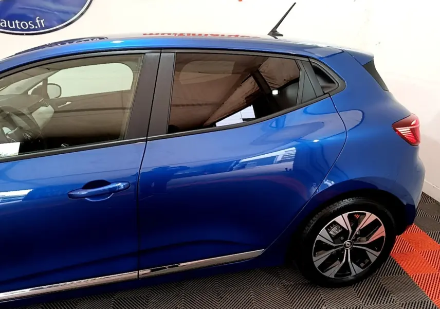 Profil côté gauche d'une Renault Clio bleu 2022 avec jantes alliage et poignées de porte ton caisse.