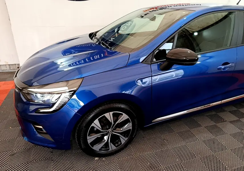 Vue 3/4 avant droit d'une Renault Clio bleu brillant avec jantes alliage et rétroviseurs noirs ton caisse.