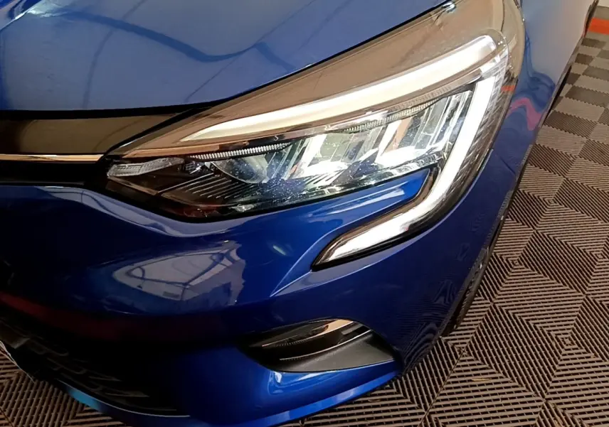 Gros plan sur le phare avant droit de la Renault Clio Evolution bleu, mettant en valeur les feux LED et la carrosserie brillante.