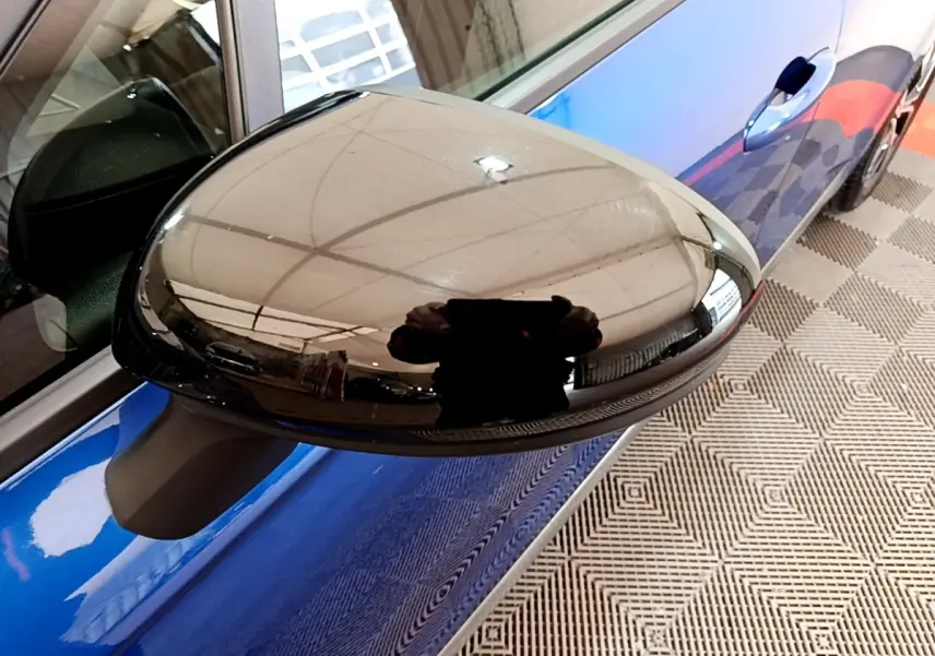 Rétroviseur droit noir brillant d’une Renault Clio bleu, vue rapprochée côté passager.