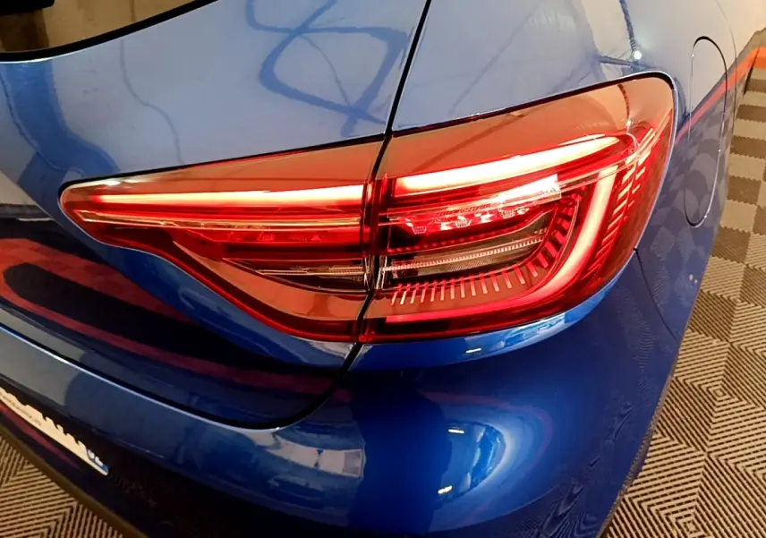Gros plan sur le feu arrière droit rouge d’une Renault Clio bleu électrique, avec la carrosserie brillante visible autour.