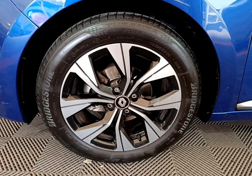 Gros plan sur la roue avant droite d’une Renault Clio bleu, jante alliage bicolore avec logo Renault central.