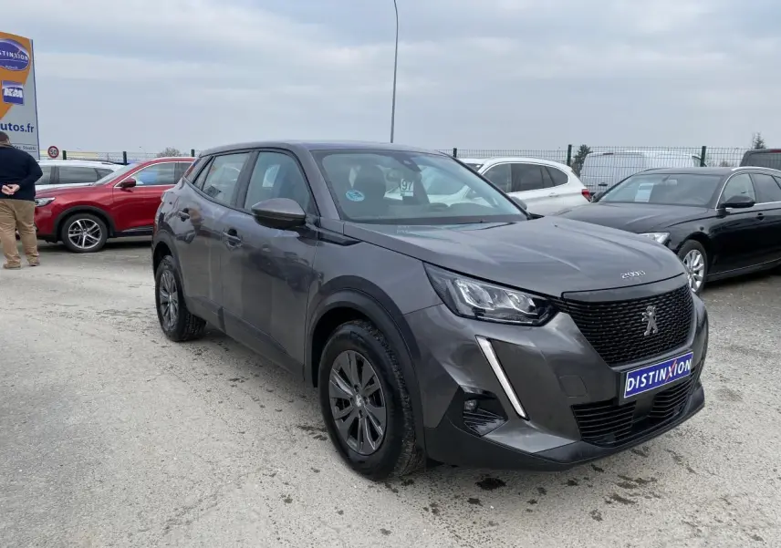 Peugeot 2008 gris foncé en 3/4 avant droit, avec calandre noire et feux LED distinctifs visibles.