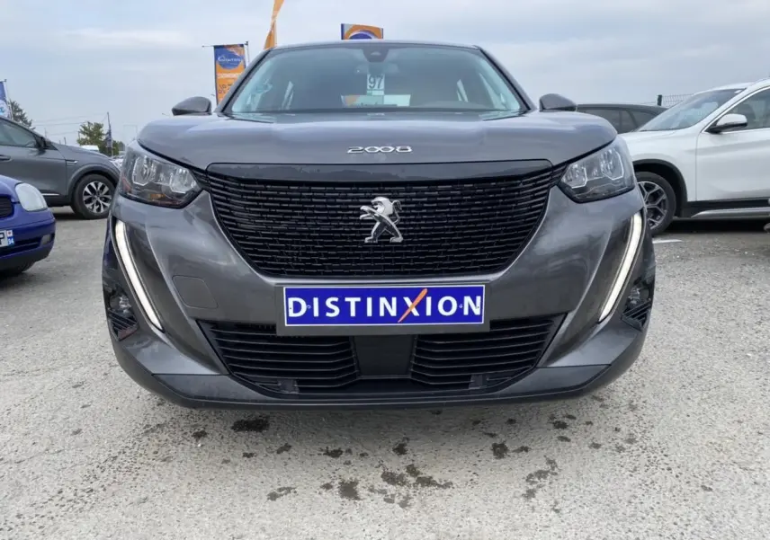 Vue frontale d'un Peugeot 2008 gris foncé avec calandre noire et feux LED en forme de griffes allumés.