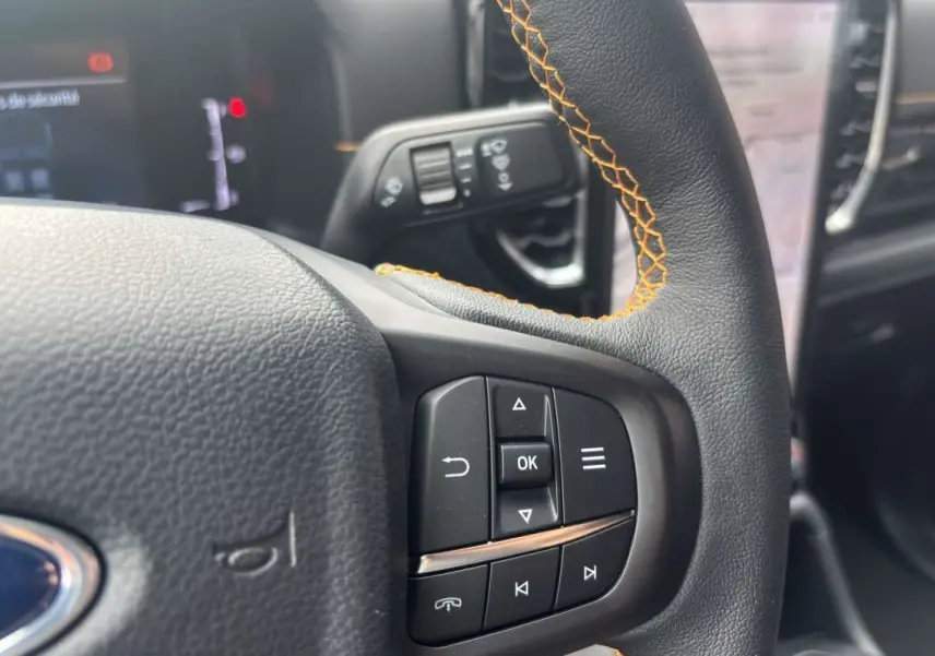 Gros plan sur le volant cuir noir avec surpiqûres orange du Ford Ranger Wildtrak 2026, boutons multifonctions visibles.