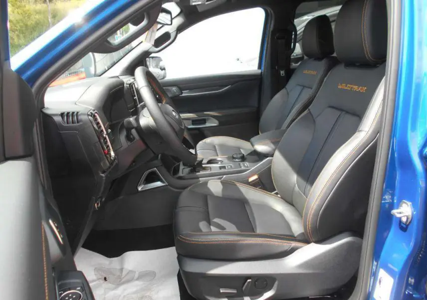 Vue intérieure côté conducteur du Ford Ranger Wildtrak Plus bleu lightning, sièges cuir noirs avec surpiqûres orange et logo Wildtrak.