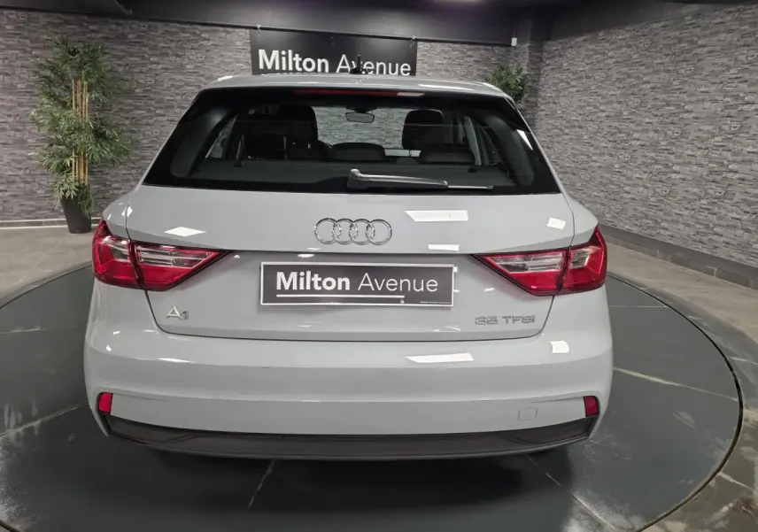 Vue arrière d'une Audi A1 Sportback gris Manhattan avec feux LED et logo Audi visible sur un plateau tournant.