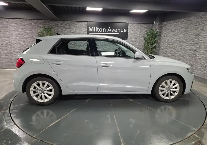Profil côté droit d'une Audi A1 Sportback 2020 gris Manhattan avec jantes aluminium 16 pouces en intérieur showroom.