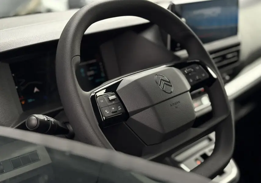 Volant noir de Citroën Jumpy 2025 avec commandes intégrées, tableau de bord numérique et écran tactile en arrière-plan.