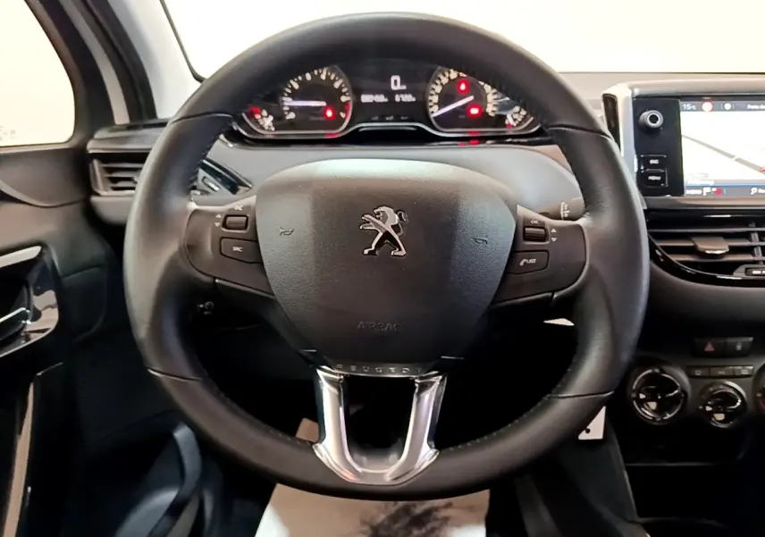 Vue intérieure centrée sur le volant noir de la Peugeot 208 avec tableau de bord et écran tactile visible à droite.