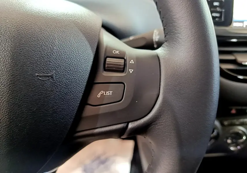 Gros plan sur le volant noir de la Peugeot 208 Puretech 82 S&S Active Business, avec commandes intégrées et tableau de bord flou en arrière-plan.