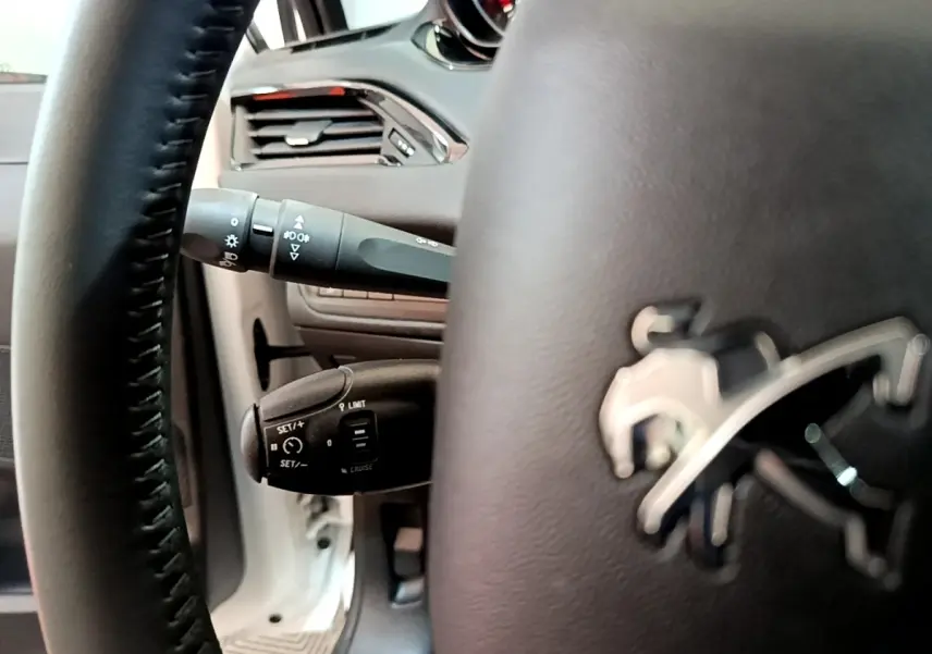 Gros plan sur le volant noir avec logo Peugeot et commandes au volant, intérieur de la Peugeot 208 blanche 2018.