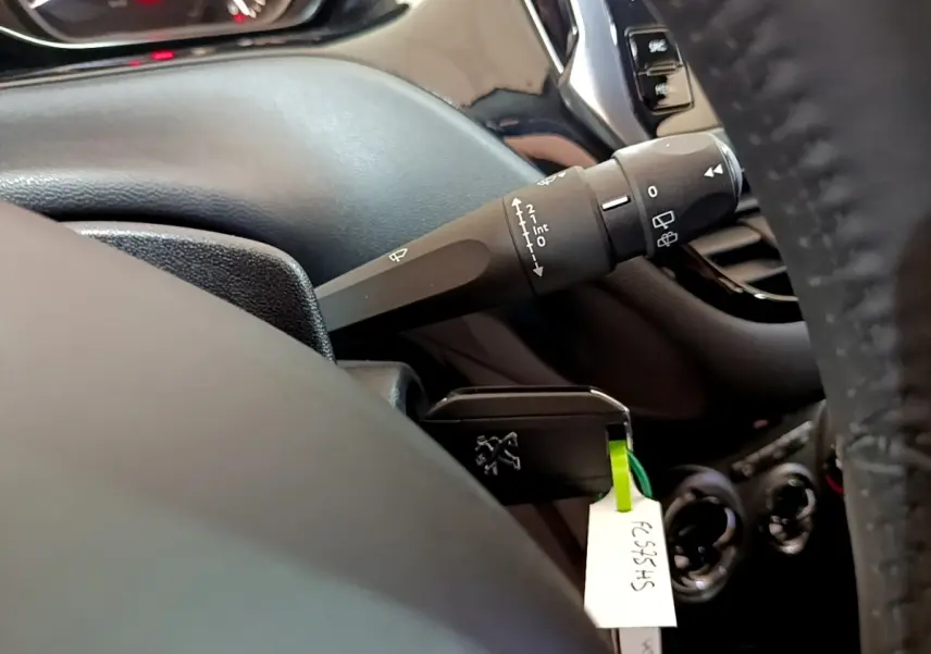 Détail intérieur du Peugeot 208 blanc de 2018 montrant la manette d’essuie-glace côté gauche et partie du tableau de bord.