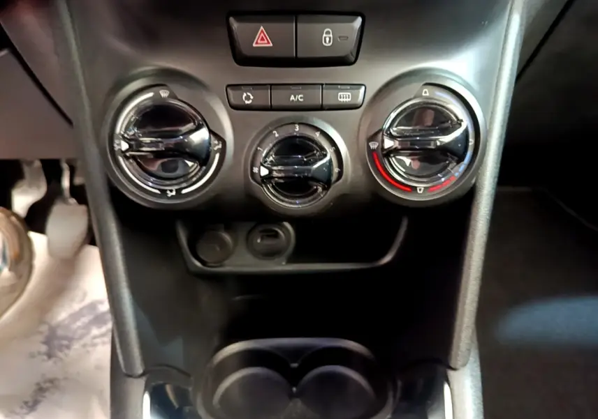 Vue rapprochée des commandes de climatisation et des boutons centraux du tableau de bord d’une Peugeot 208 blanche.