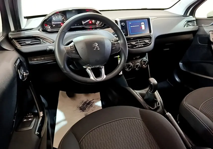 Intérieur noir Peugeot 208 Puretech 82, vue du poste de conduite avec volant, écran tactile et boîte manuelle.