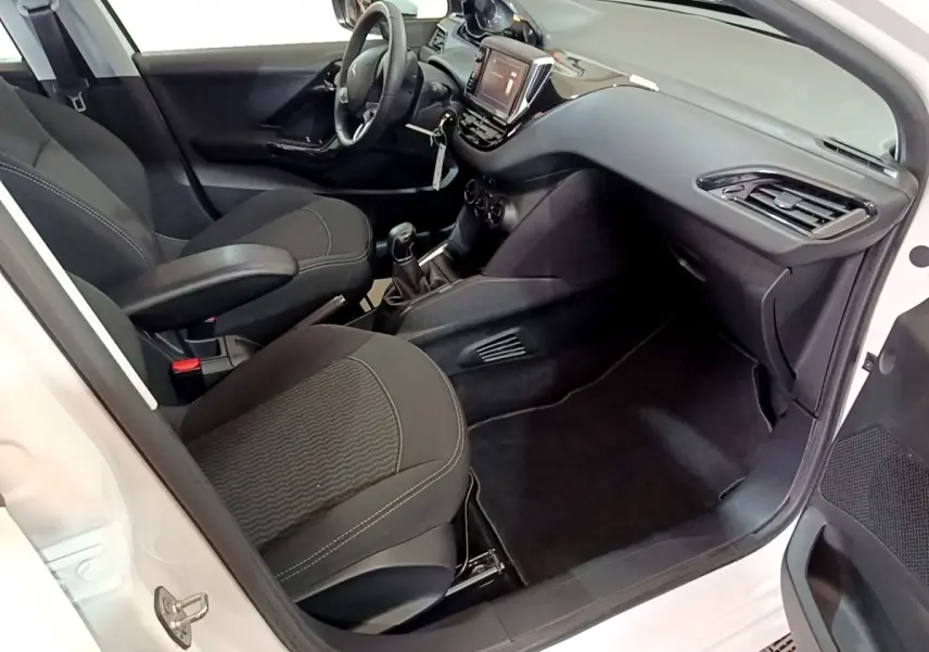 Intérieur côté passager d’une Peugeot 208 blanche, montrant les sièges noirs et le tableau de bord avec écran tactile.
