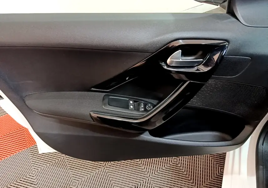 Vue rapprochée de la porte intérieure côté conducteur d’une Peugeot 208 blanche, avec poignée et commandes électriques.