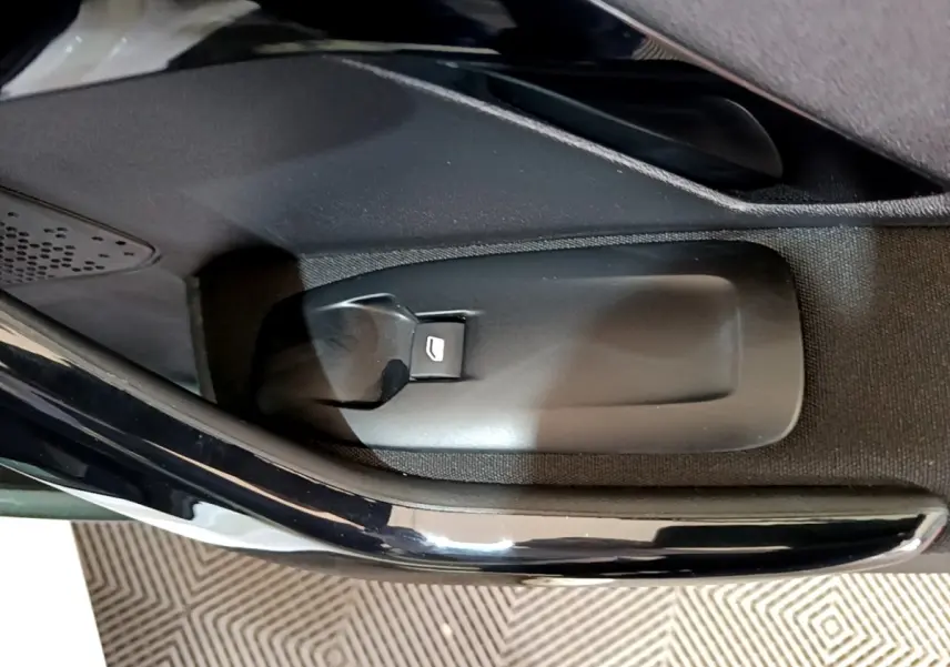 Gros plan sur le bouton d’ouverture de coffre côté intérieur d’une Peugeot 208 blanche, détail de la portière.
