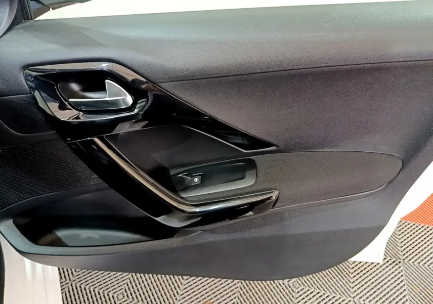 Vue rapprochée de la porte intérieure côté gauche d’une Peugeot 208 blanche, avec poignée noire brillante.