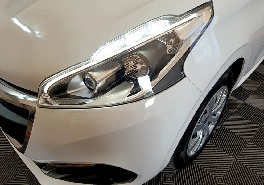 Gros plan sur l’avant droit blanc d’une Peugeot 208 2018, mettant en valeur le phare et la roue.
