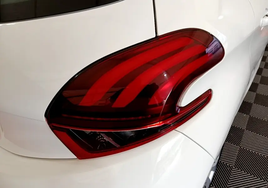 Gros plan sur le feu arrière droit rouge d’une Peugeot 208 blanche vue de l’arrière côté droit.