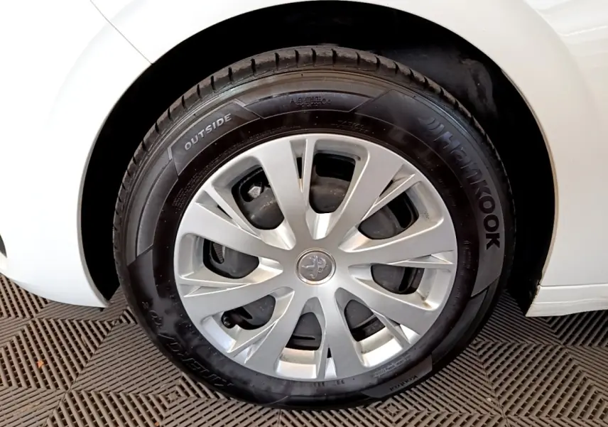 Gros plan sur la roue avant droite d'une Peugeot 208 blanche, mettant en valeur la jante et le pneu Hankook.