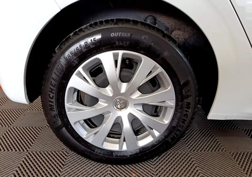 Gros plan sur la roue avant droite d'une Peugeot 208 blanche, avec jante argentée et pneu Michelin visible.