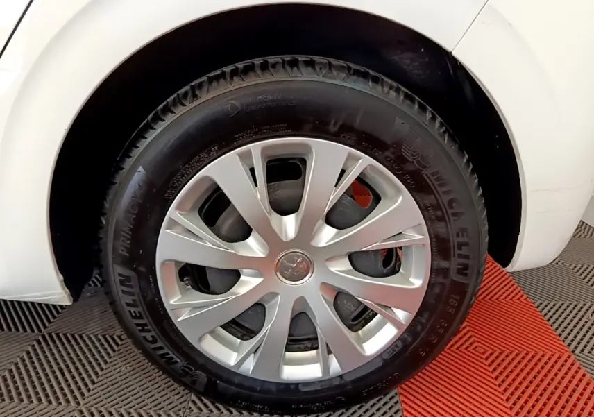 Gros plan sur la roue avant gauche d'une Peugeot 208 blanche, avec jante argentée et pneu Michelin.