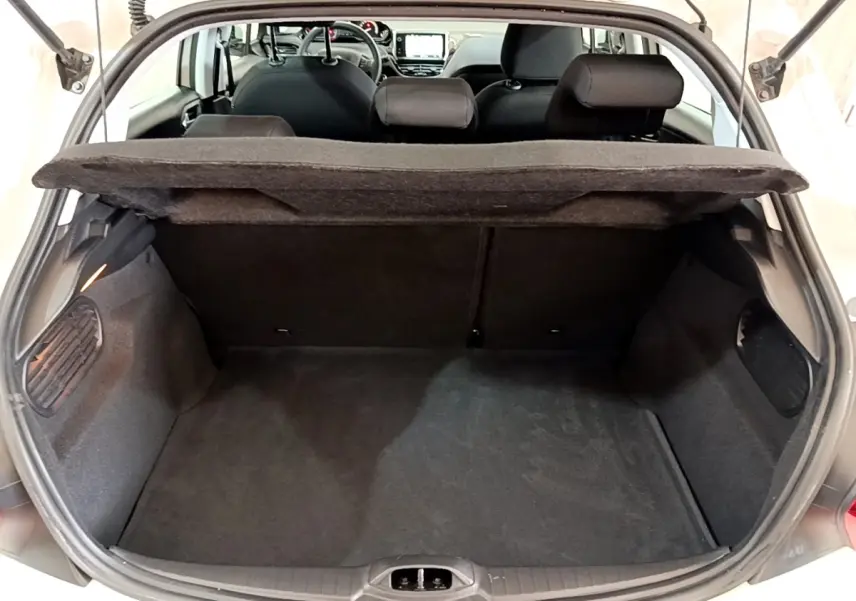 Vue arrière du coffre ouvert d'une Peugeot 208 blanche, montrant l'espace de chargement et la tablette arrière relevée.