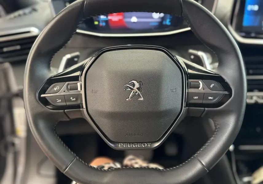 Gros plan sur le volant cuir noir du Peugeot 2008 2023 avec commandes intégrées et logo lion central.