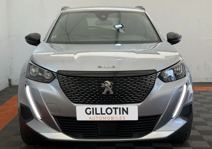 Vue frontale d'un Peugeot 2008 gris clair avec calandre noire et feux LED verticaux allumés.