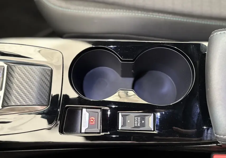 Gros plan sur la console centrale noire brillante du Peugeot 2008 gris clair, avec porte-gobelets et commandes Drive Mode et frein à main électrique.