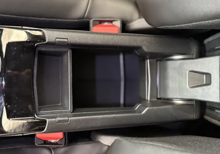 Vue plongeante sur la console centrale noire du Peugeot 2008 gris clair, avec rangement ouvert entre les sièges avant.