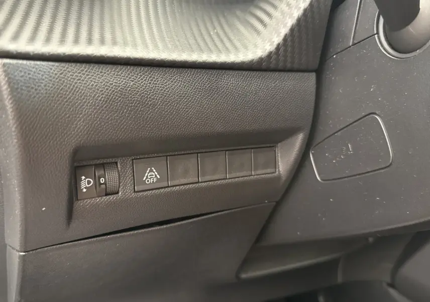 Détail intérieur côté gauche du tableau de bord noir avec commandes de réglage des phares et d'alerte de franchissement de ligne.