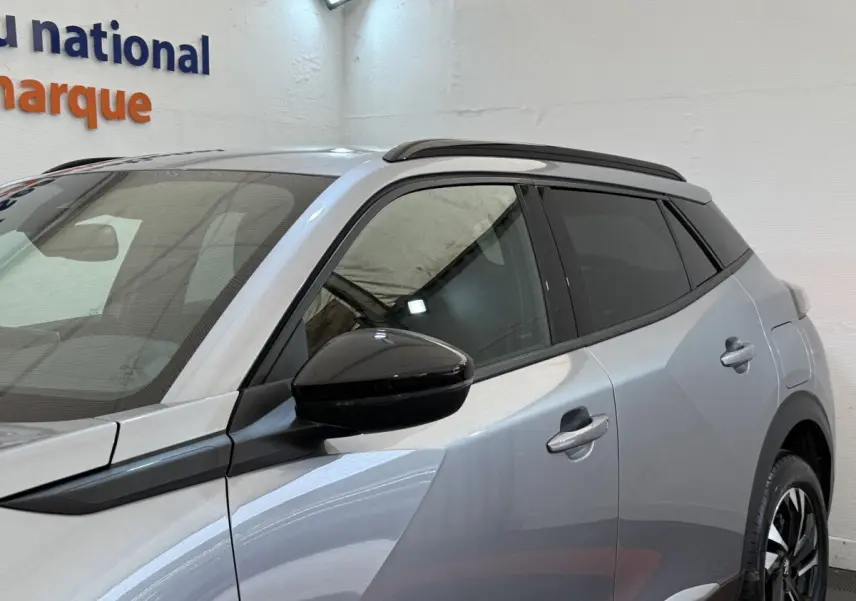 Vue de côté droit 3/4 arrière d’un Peugeot 2008 gris clair avec rétroviseur noir et toit noir contrasté.