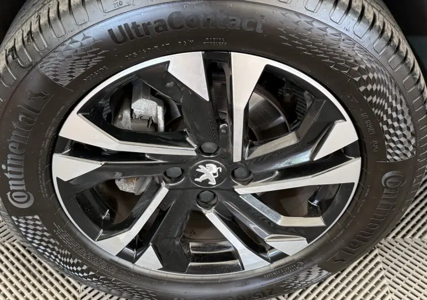 Gros plan sur la jante alliage bicolore noire et argentée avec logo Peugeot au centre, montée sur pneu Continental.