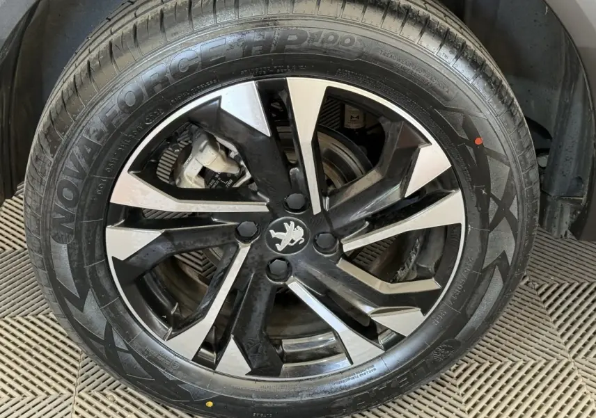 Gros plan sur la jante alliage noire et argentée avec logo Peugeot au centre, montée sur un pneu neuf.