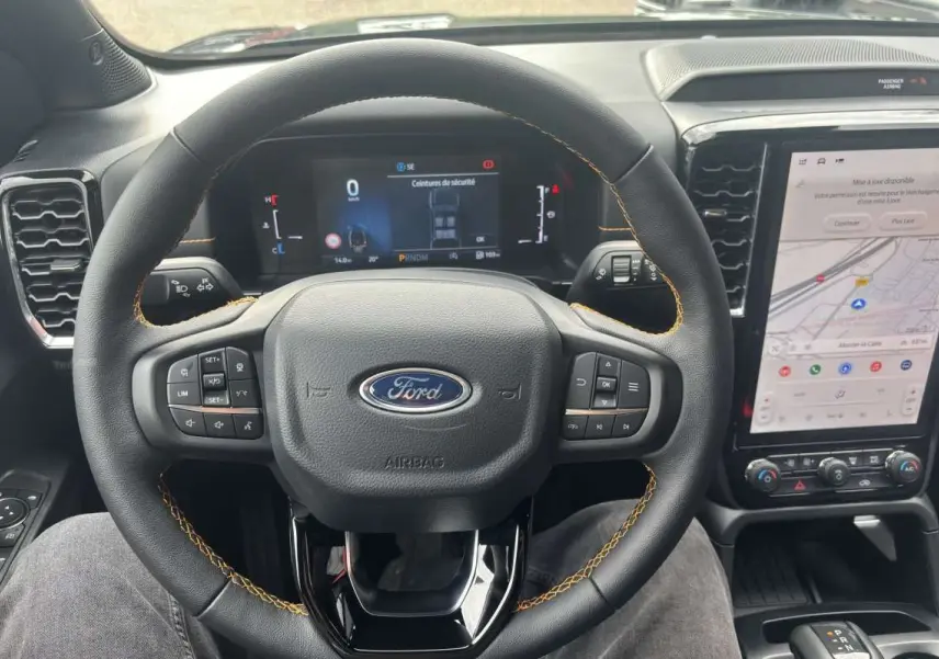 Vue intérieure centrée sur le volant cuir noir avec surpiqûres orange du Ford Ranger 2026 et écran tactile vertical.