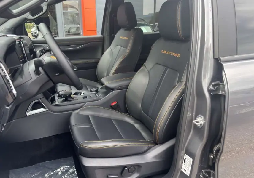 Vue intérieure côté conducteur du Ford Ranger Wildtrak 2026 gris carbone, sièges cuir noirs avec surpiqûres orange et logo Wildtrak brodé.