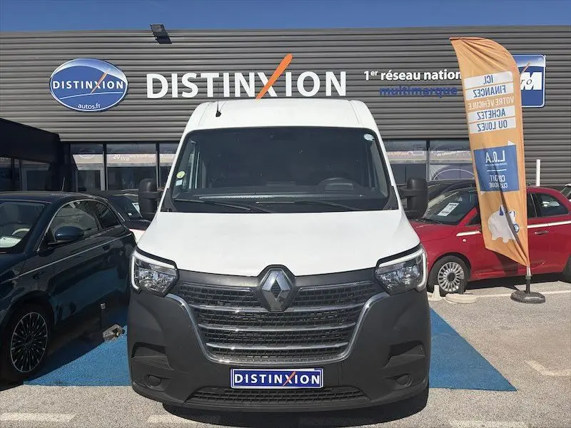 Vue de face d’un Renault Master blanc stationné devant un concessionnaire Distinxion avec une bannière orange à droite.