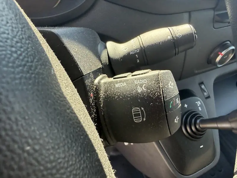 Gros plan sur la commande multimédia noire à gauche du volant dans l'habitacle d'un Renault Master blanc.