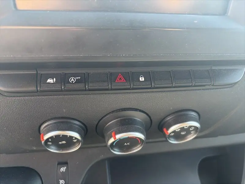 Gros plan sur les commandes de climatisation et les boutons de sécurité du tableau de bord du Renault Master blanc.