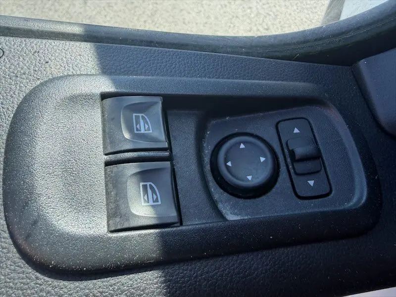 Gros plan sur les commandes de lève-vitres et réglage des rétroviseurs côté conducteur du Renault Master blanc.