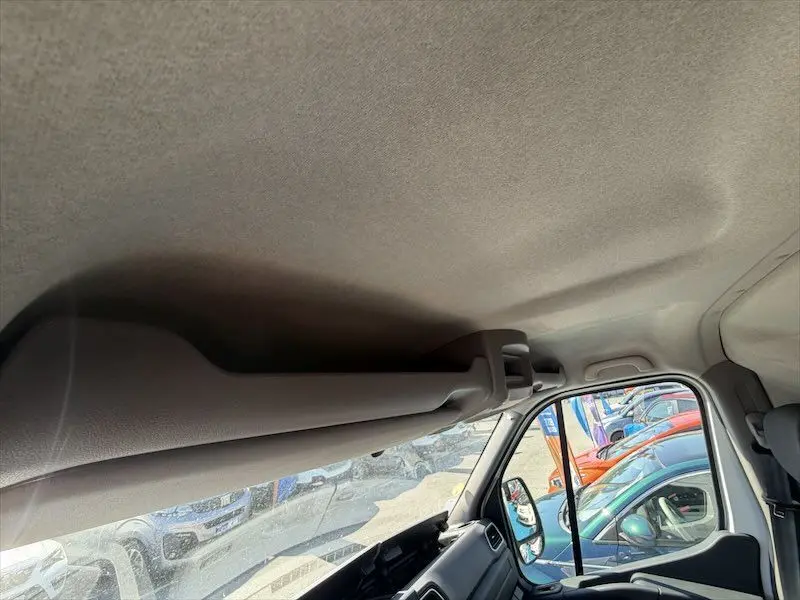 Vue intérieure côté passager du toit et pare-soleil du Renault Master blanc, avec reflet de véhicules garés à l'extérieur.